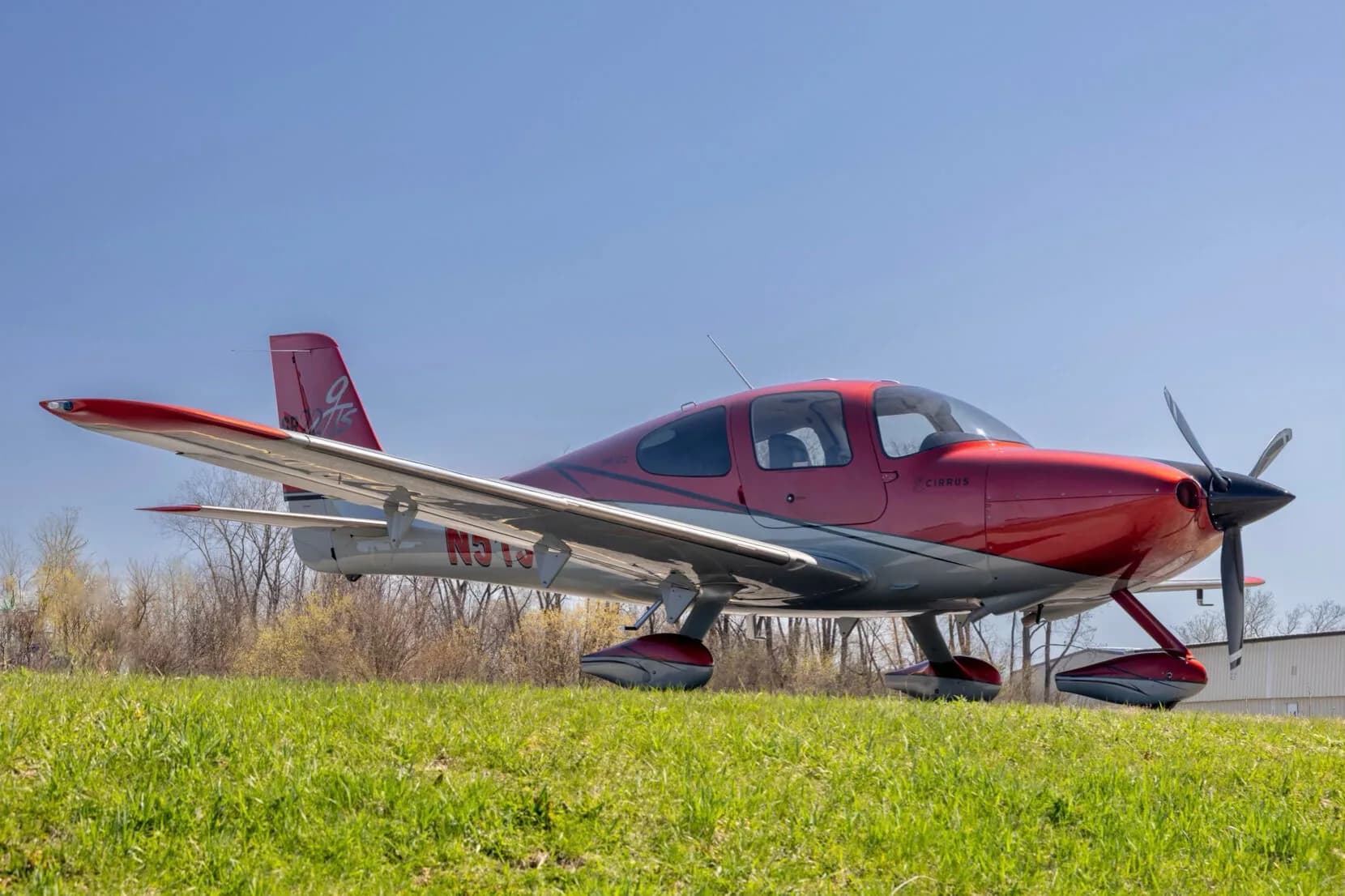 A red and grey Cirrus SR22T aircraft (N513Z) parked on a grassy field from a low angle.