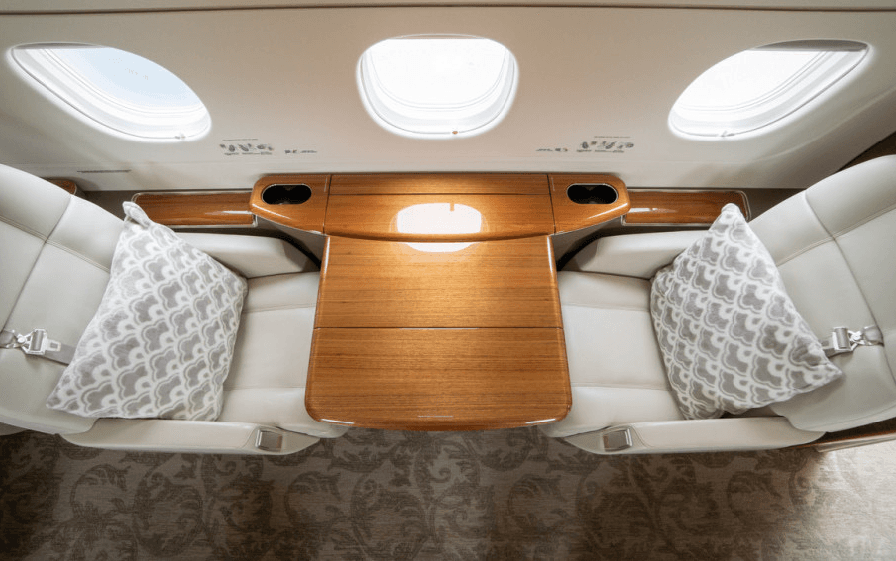 An overhead view of two light-colored leather seats facing each other, separated by a polished wooden table with cupholders.