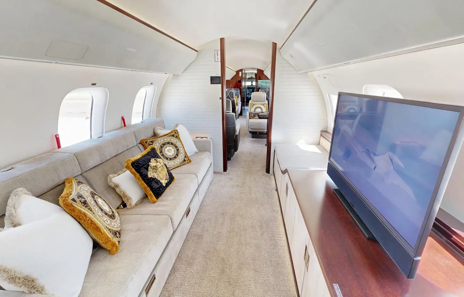 A section of the private jet cabin with a long grey sofa adorned with Versace pillows and a large flat-screen television.