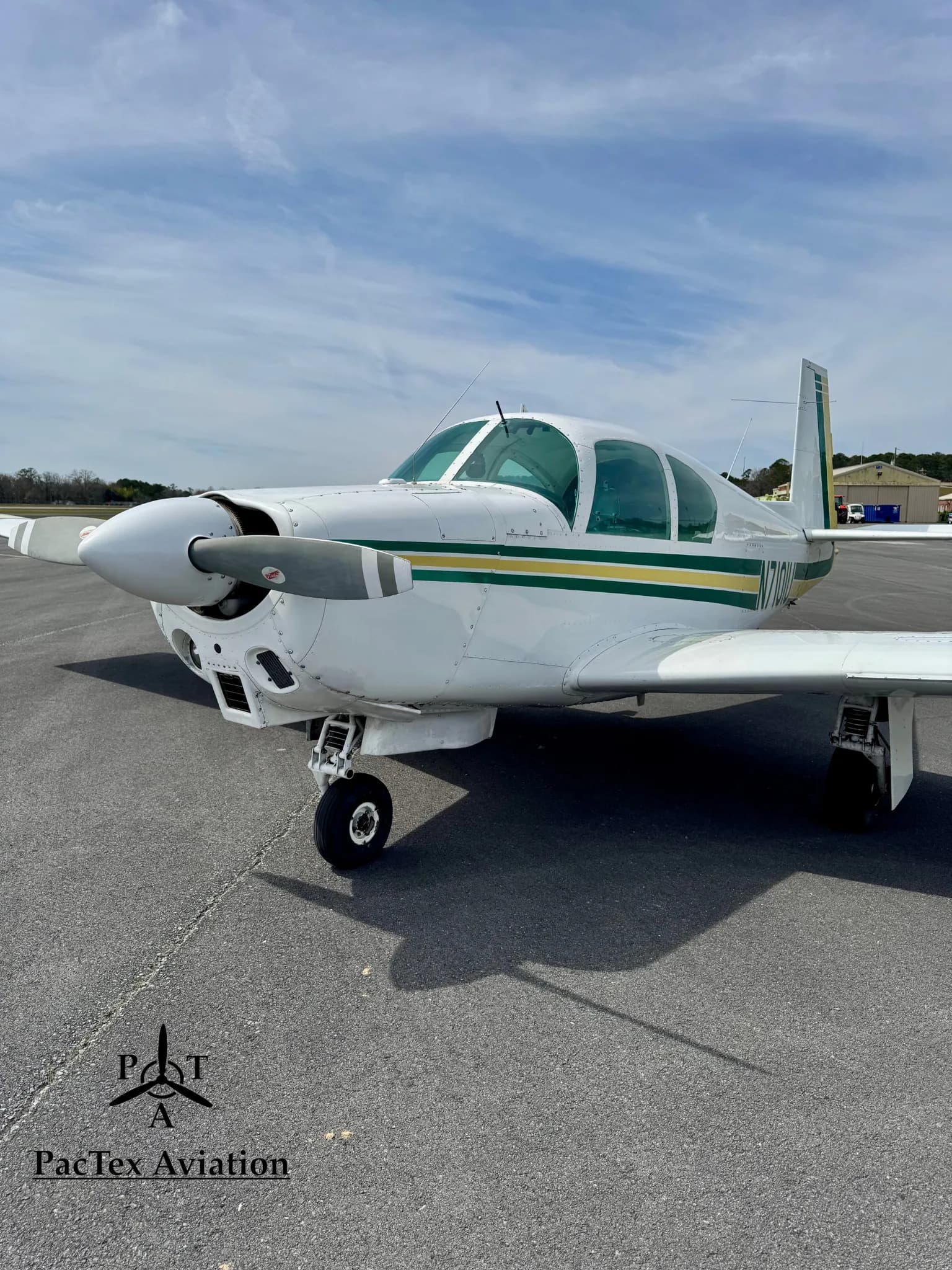A close-up front view of a white Mooney M20C aircraft with green and yellow stripes, showing the propeller and nose gear.