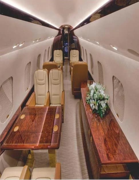 A long view of a private jet's luxurious cabin with a dining table, comfortable seating, and a side console with flowers.