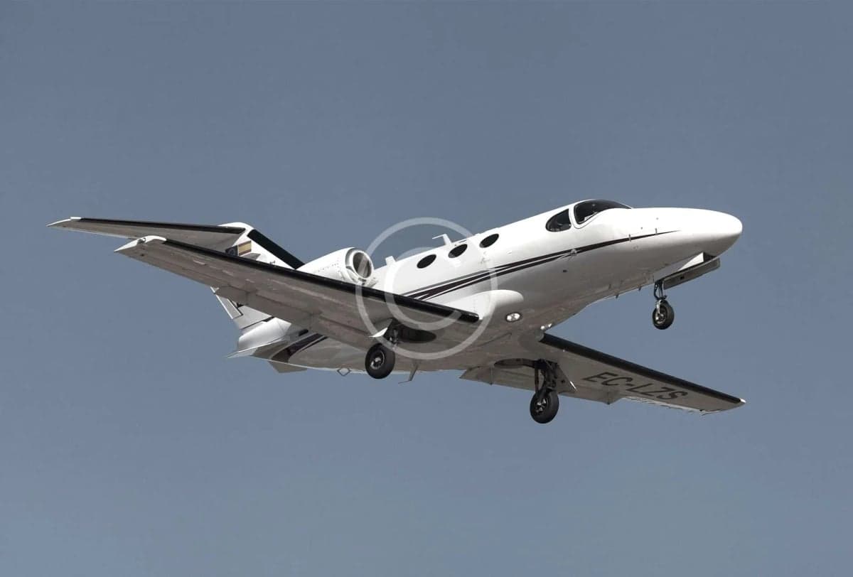 A white Cessna Citation CJ3 is shown in flight with its landing gear down.