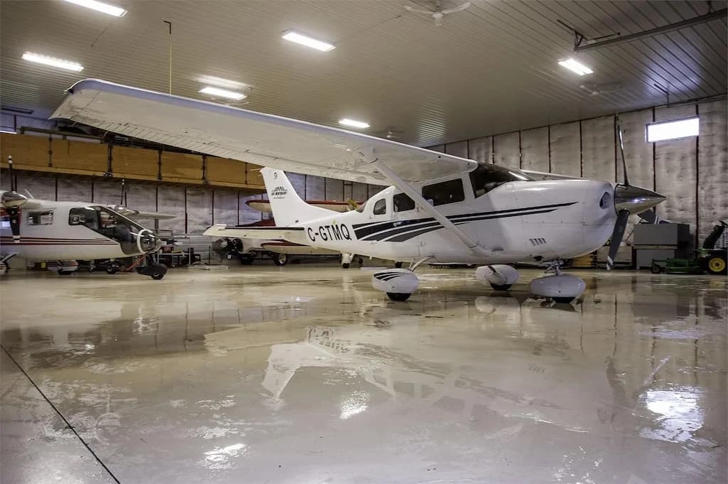 A white single-engine propeller aircraft, registration C-GTMQ, parked inside a brightly lit hangar with a reflective floor.