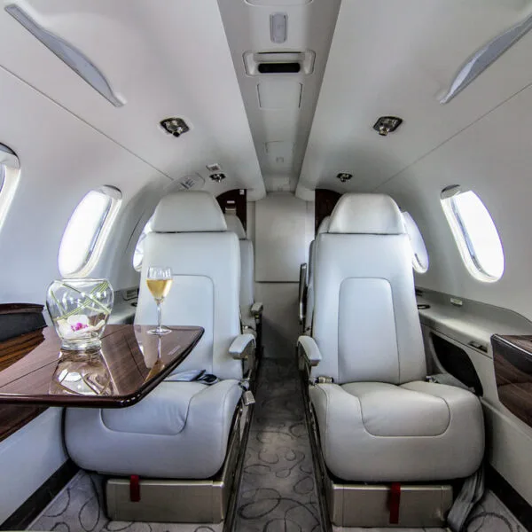 A luxurious aircraft cabin interior with light grey leather seats and a table set with champagne.