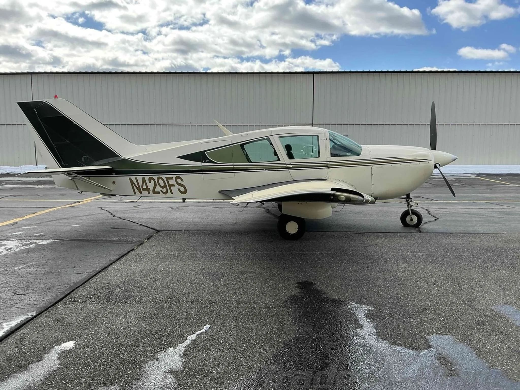 A side profile view of the white and green Bellanca Viking aircraft, N429FS, parked on an asphalt ramp.