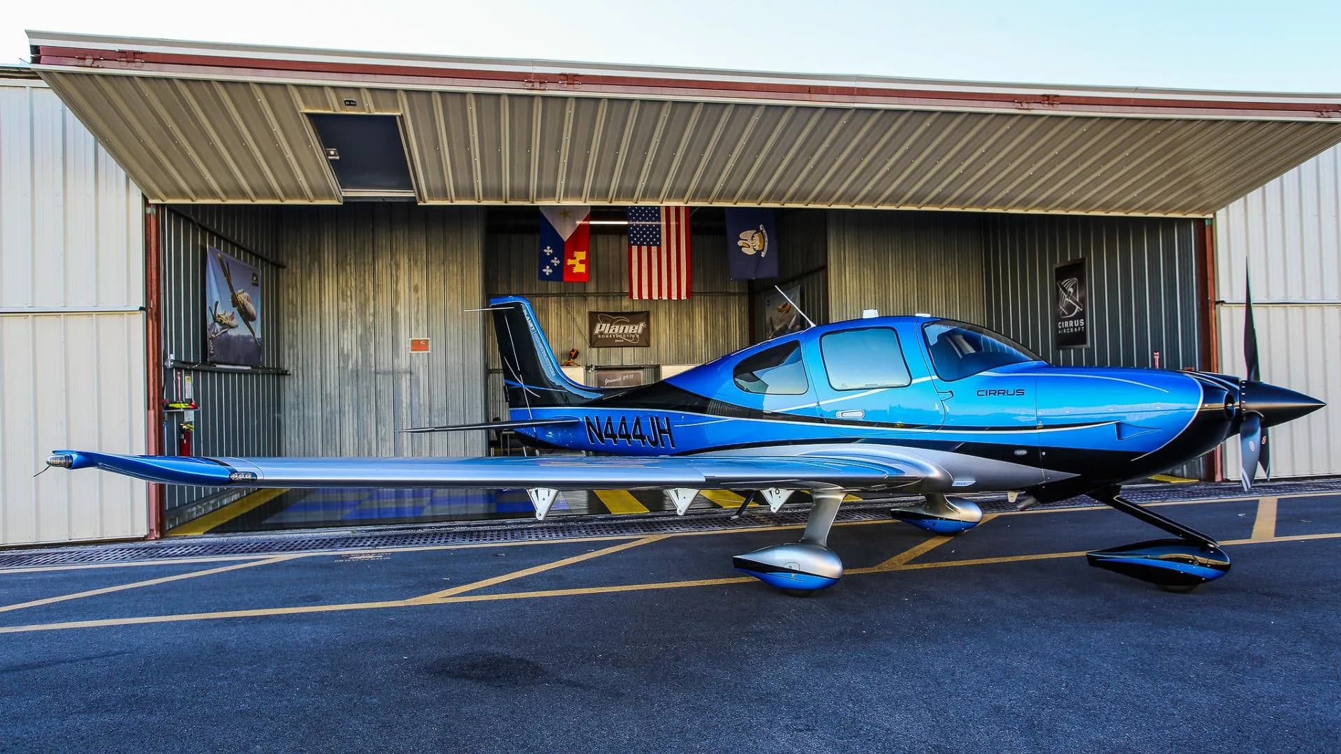 A blue and silver Cirrus SR22 aircraft with registration N444JH parked outside a hangar.