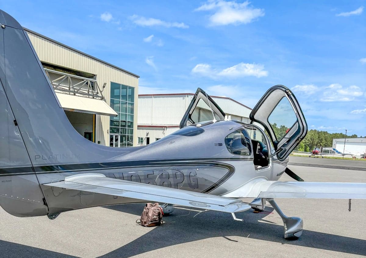 A Cirrus SR22T aircraft is parked on the tarmac with its gull-wing doors open.