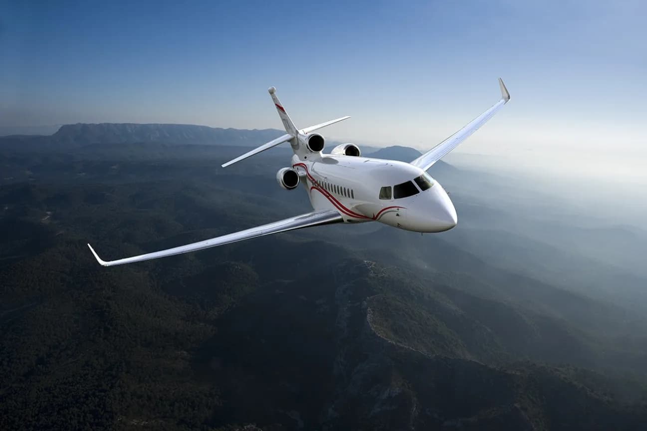 Front view of a white jet aircraft in flight over a mountainous landscape.