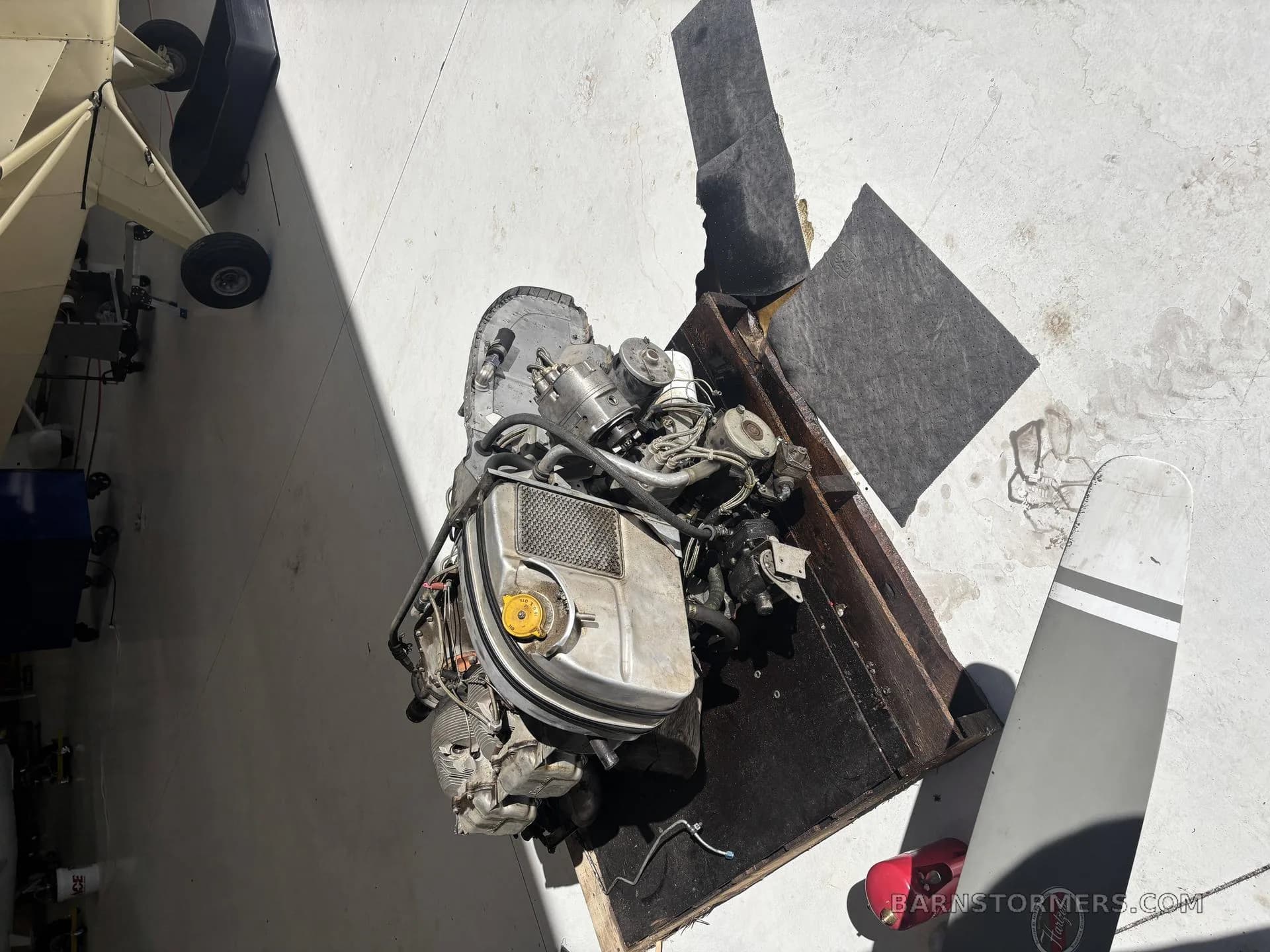 An overhead view of an aircraft engine on a wooden stand, with a light-colored aircraft wing visible in the background.