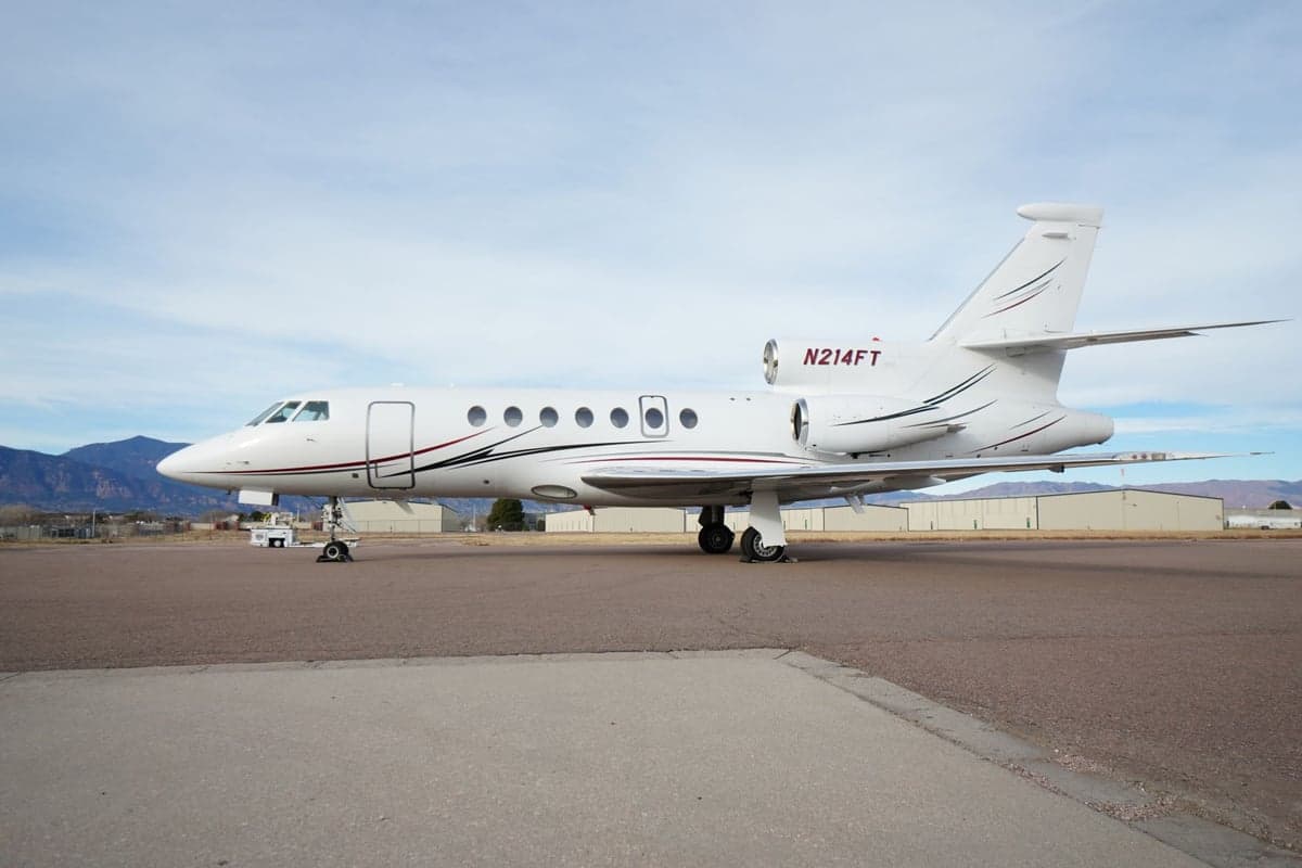 A white Falcon jet with registration N214FT is parked on the tarmac.