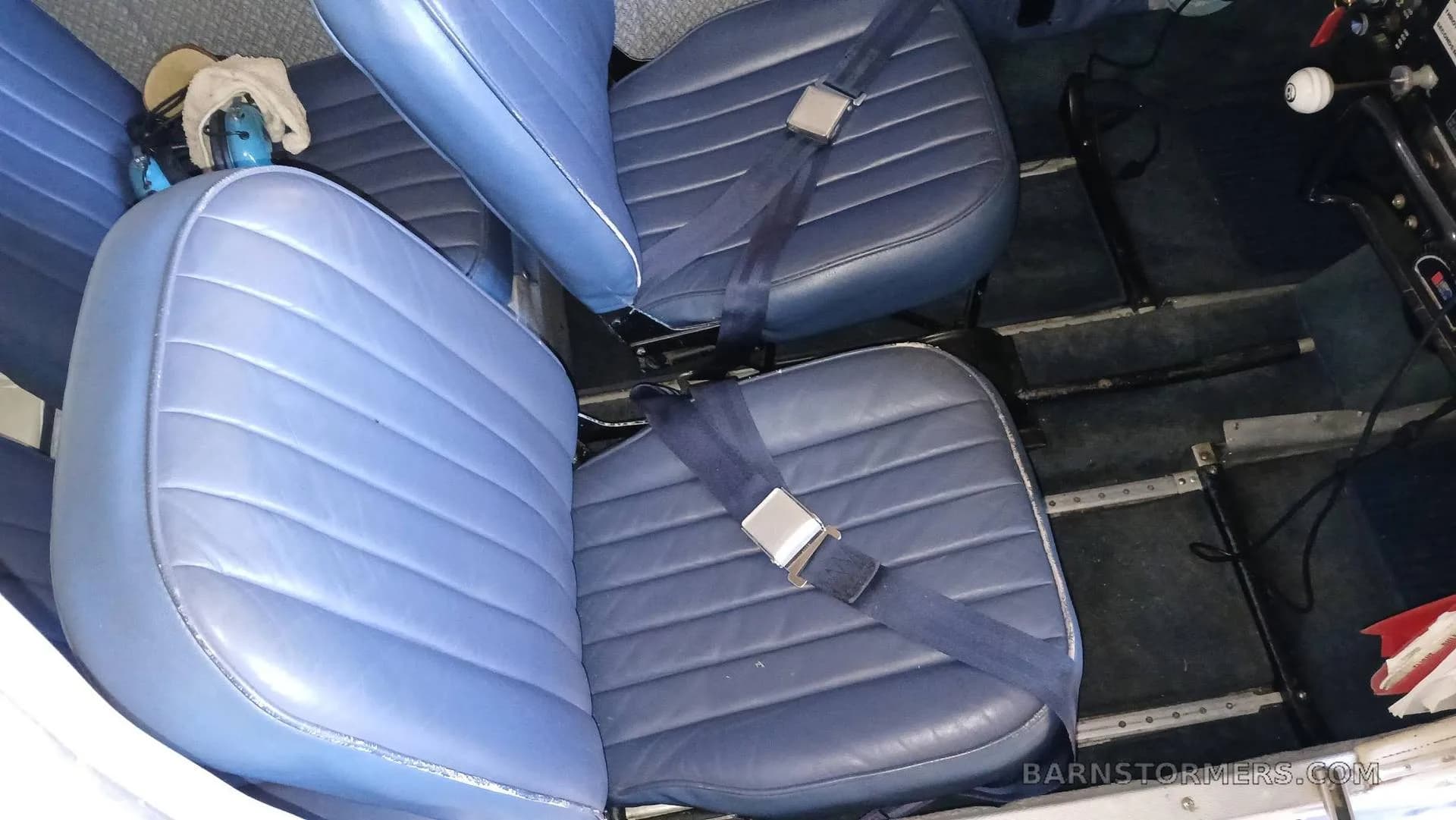 Two blue vinyl aircraft seats with seatbelts in the cabin.