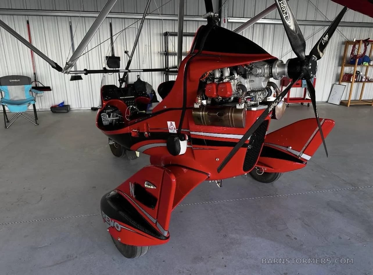 A red weight-shift control aircraft with its engine exposed is parked inside a hangar.