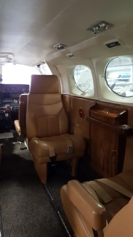 The tan leather interior cabin of a private aircraft with a small table and multiple seats.