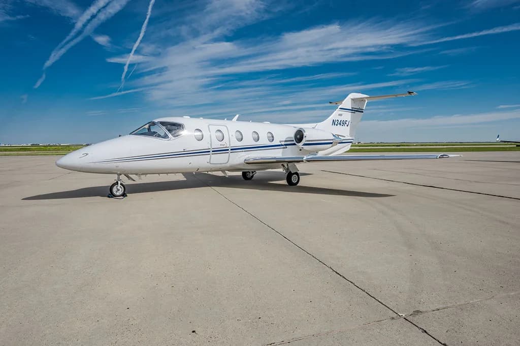 A white business jet with blue stripes, registration N349FJ, parked on an airport tarmac under a blue sky.