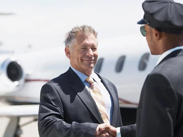 A businessman shakes hands with a pilot in front of a private jet.