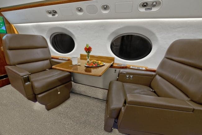 Close-up of the aircraft interior with leather seats and a table set for a meal.
