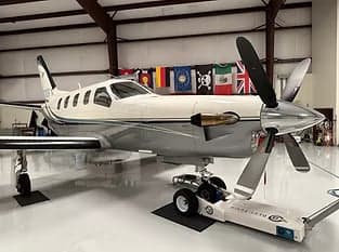 Side view of a turboprop aircraft in a hangar with flags in the background.