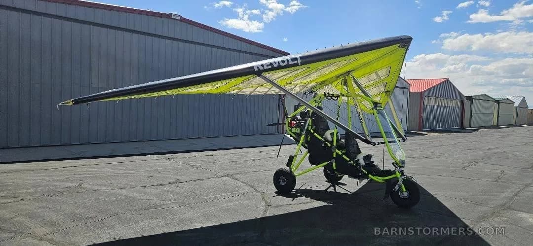 A three-quarter rear view of a yellow and black Revolt ultralight trike on an airfield tarmac.