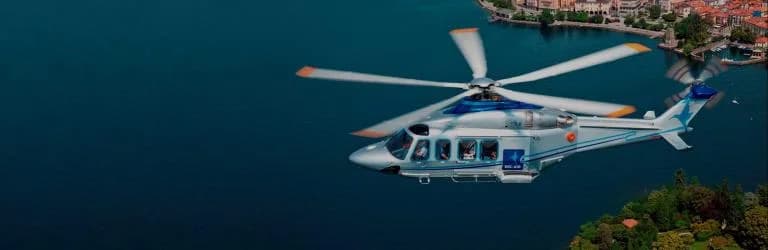 AgustaWestland AW169 helicopter flying over a lake near a town.