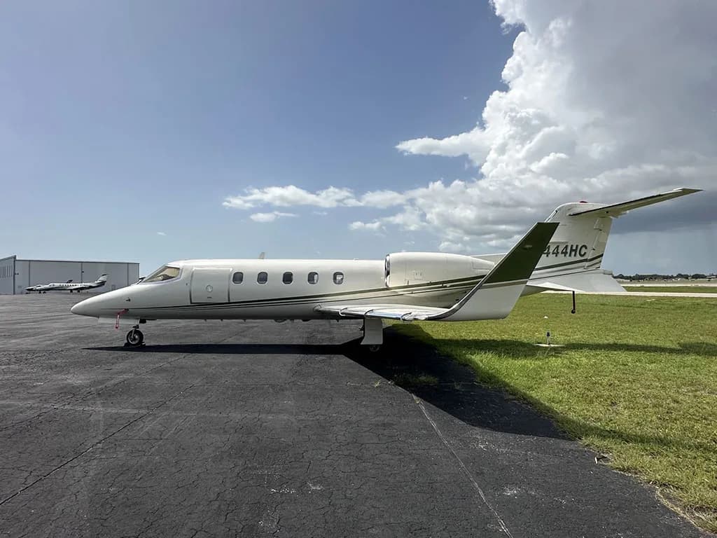A white Learjet 35A with N444HC on the tail, parked on an asphalt ramp next to grass and a hangar.