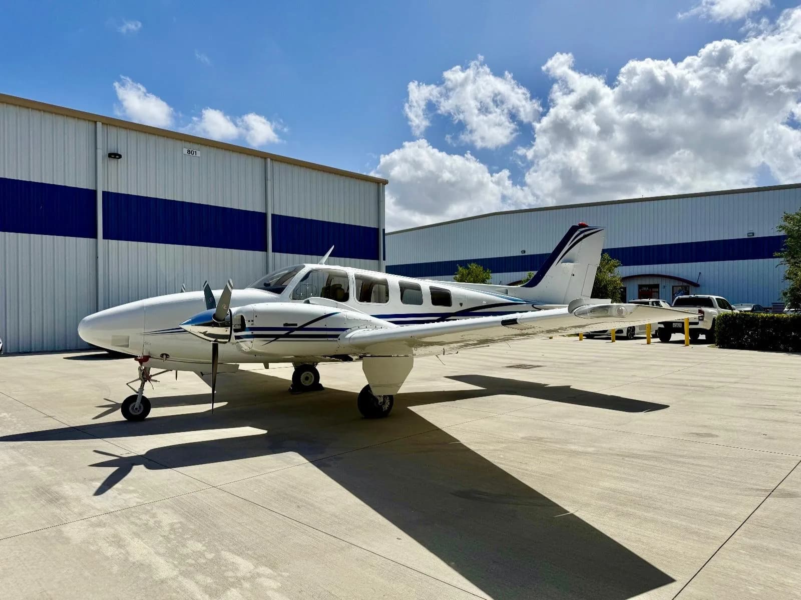 A white and blue twin-engine aircraft is parked on the tarmac in front of a hangar.