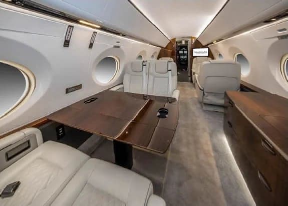 Aircraft interior with cream-colored leather seats and a wood table.