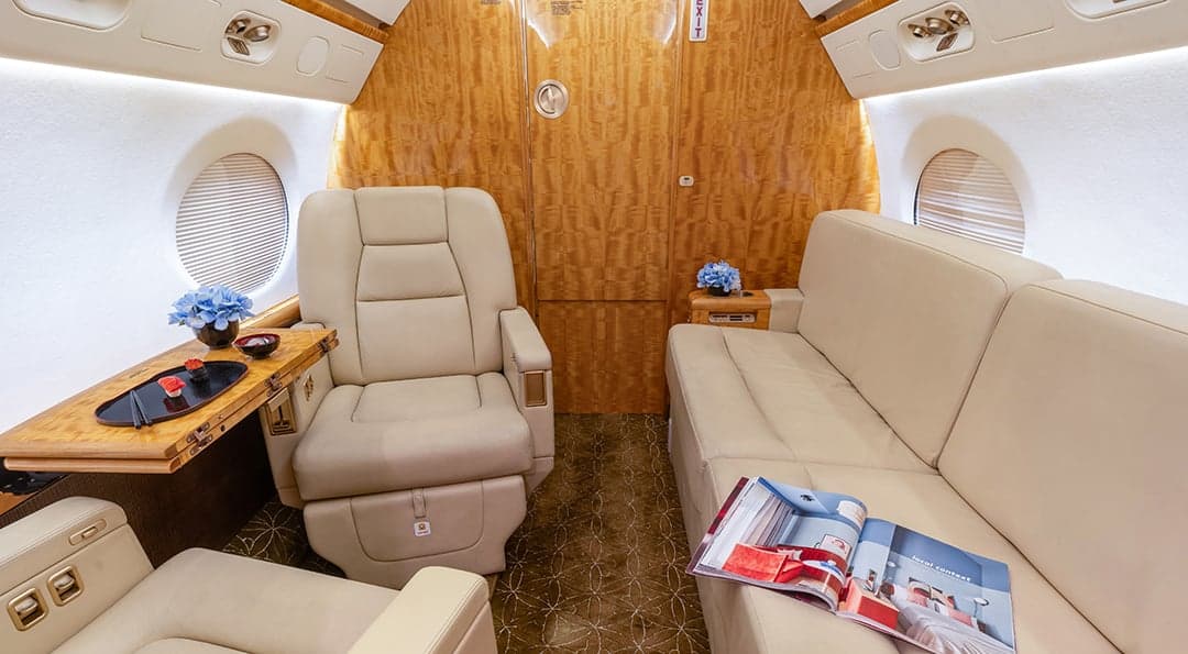 The aircraft's interior features cream-colored leather seats and wood paneling, with a magazine and flowers on display.