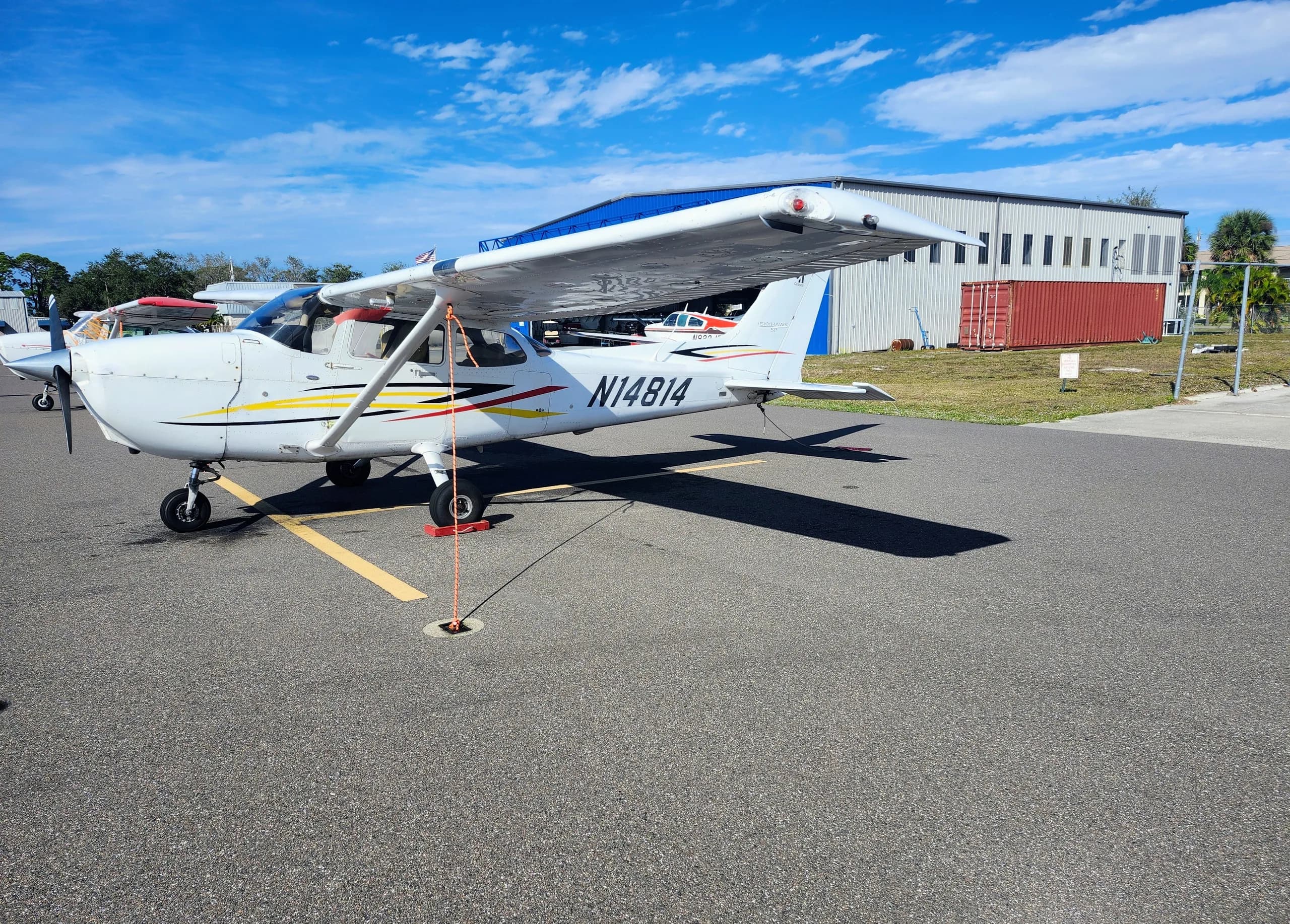 A white Cessna N14814 aircraft is parked on an airport tarmac next to a blue hangar building.