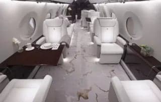 A view of the aircraft's interior with white leather seats, a table, and marble flooring.