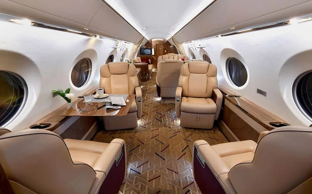 The luxurious interior cabin of a private jet with beige leather seats and a patterned carpet.