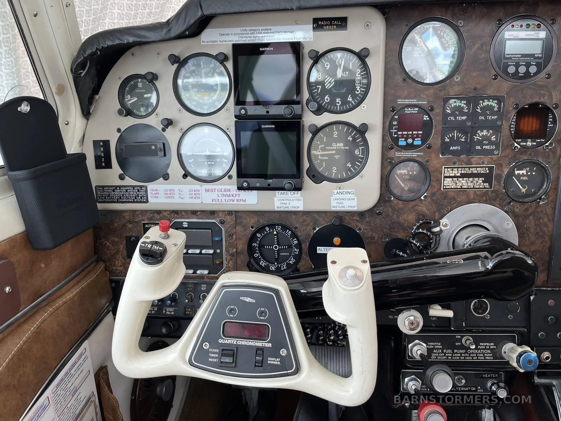 A close-up view of the Beechcraft Bonanza cockpit, focusing on the instrument panel with various gauges, Garmin displays, and the white control yoke.