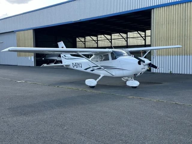 A white single-engine propeller aircraft with black stripes, registration D-EIYJ, parked on an asphalt apron in front of a hangar.
