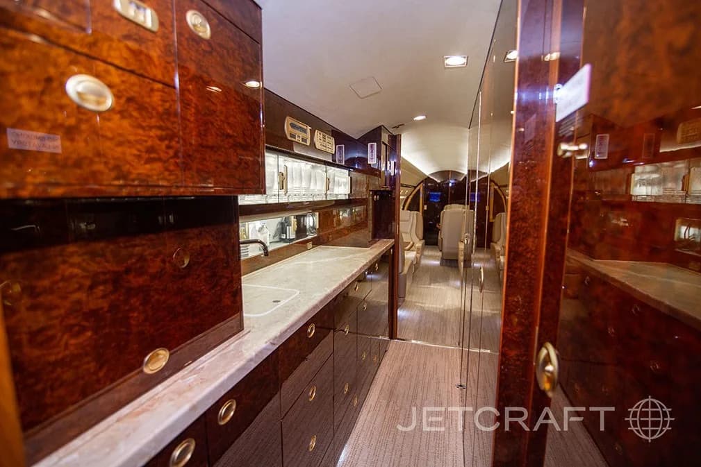 The galley area of a private jet with dark wood cabinetry, a marble countertop, and glassware storage.