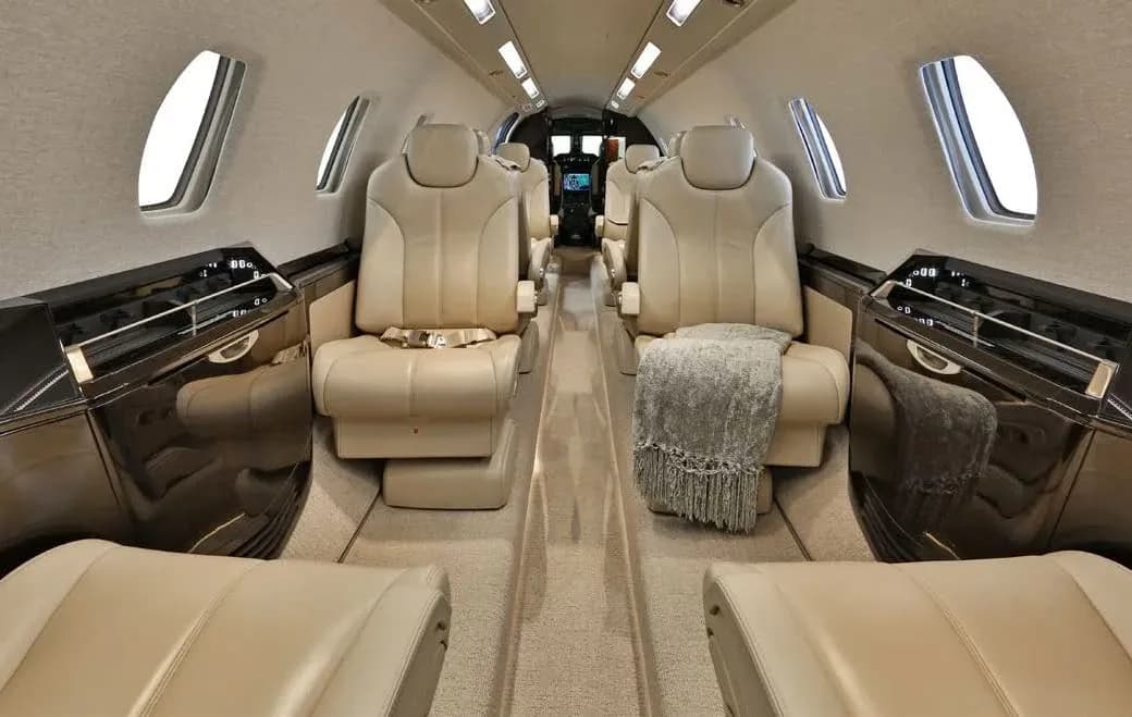 The luxurious cabin interior of a business jet, featuring tan leather seats and a gray blanket on one seat.