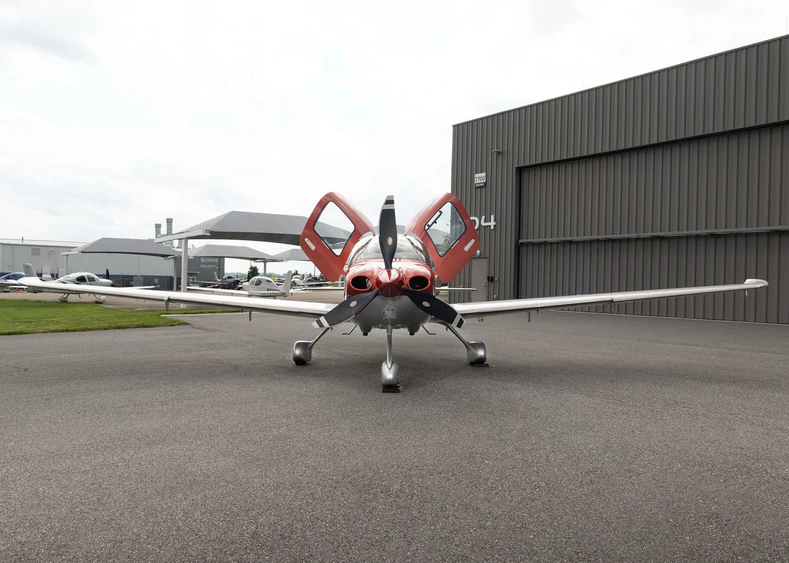 A front view of a red and silver Cirrus SR22T aircraft, registration N96KJ, with its gull-wing doors open, parked on an apron.