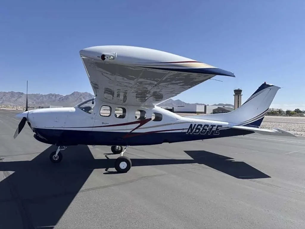A white and blue Cessna 210 Centurion with registration N66TE parked on an airfield under a clear sky.