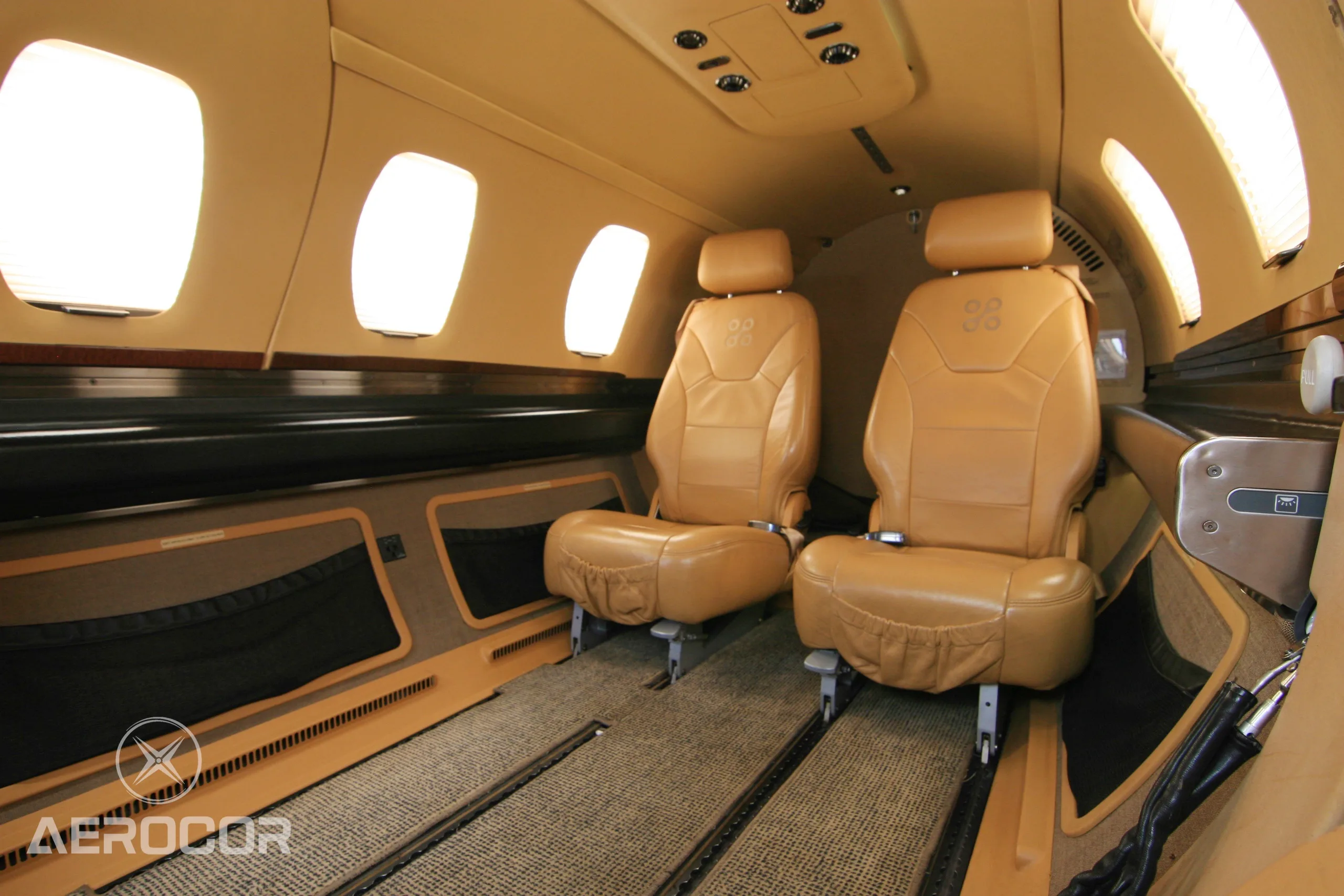The tan leather interior cabin of an Eclipse 500 jet, showing two passenger seats and windows.