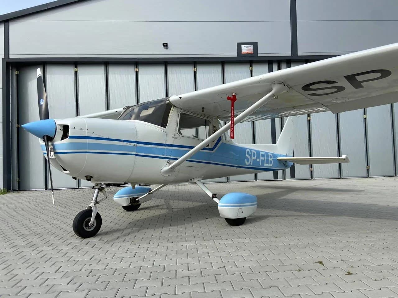 Side view of a Cessna 150 with blue and white paint scheme parked in front of a hangar.