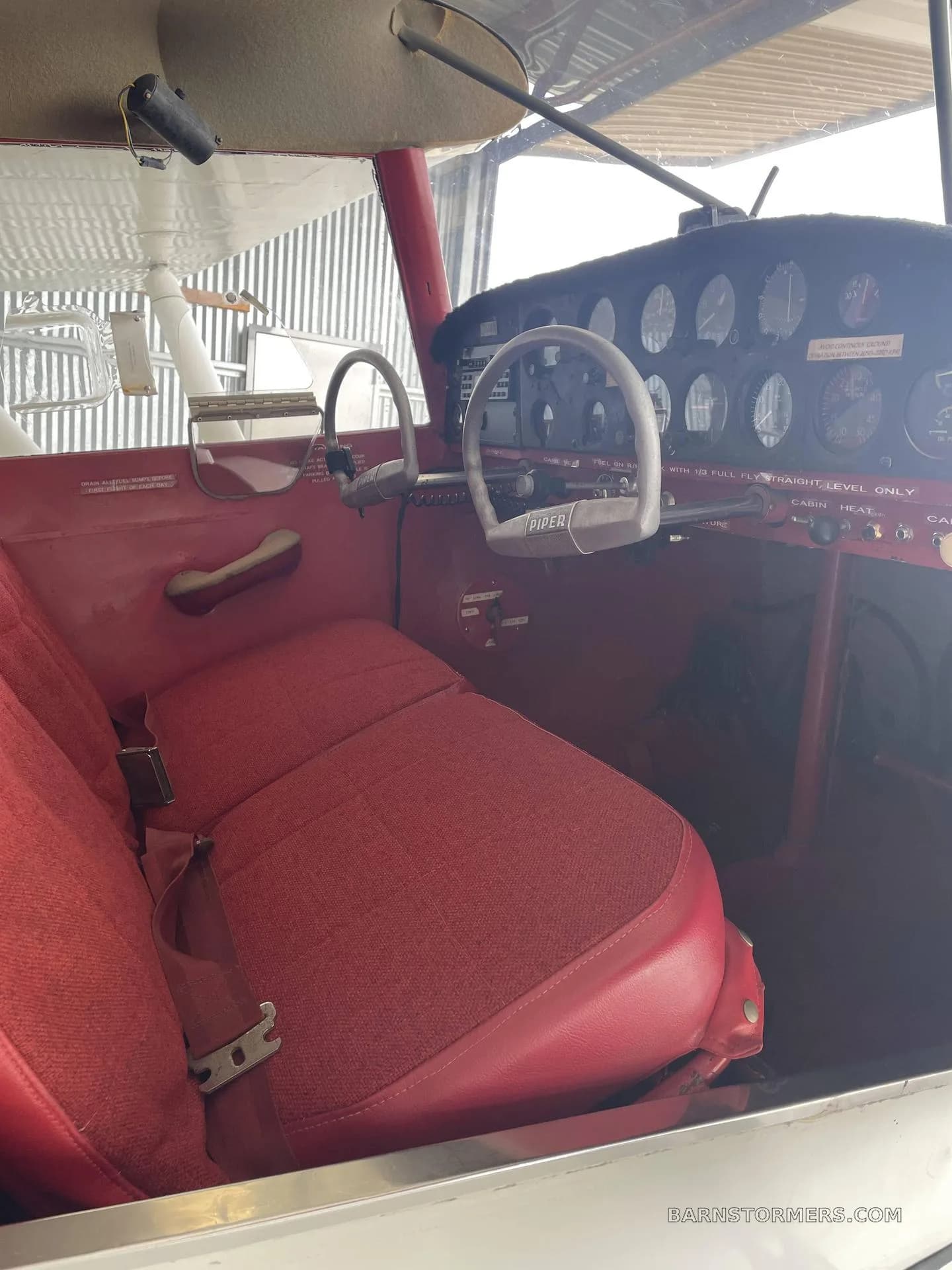 The red fabric interior cabin and instrument panel of a Piper aircraft.