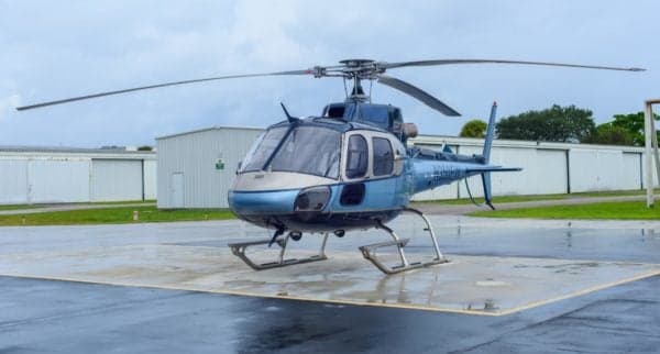 A Eurocopter AS350B3 Ecureuil helicopter is parked on a wet tarmac.
