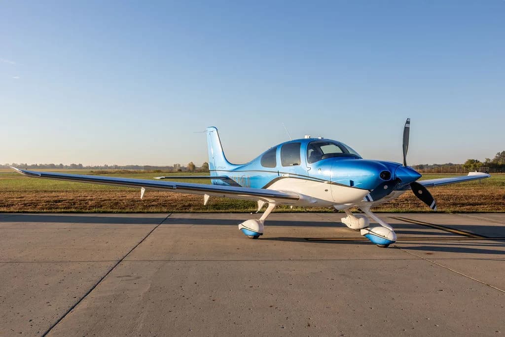 A blue and white Cirrus SR22 aircraft parked on an airfield with a clear sky.