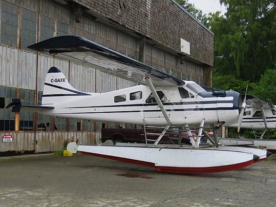 A white and blue floatplane is parked in front of a hangar.