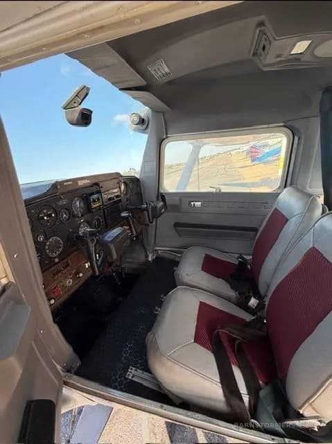 The interior cabin of a small aircraft, showing two grey and red seats and the cockpit panel.