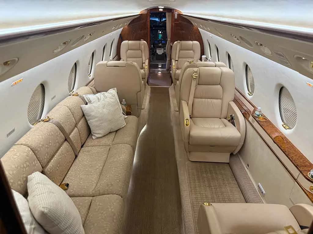A wider view of the business jet's cabin interior, showing a beige sofa on the left and individual seats on the right.