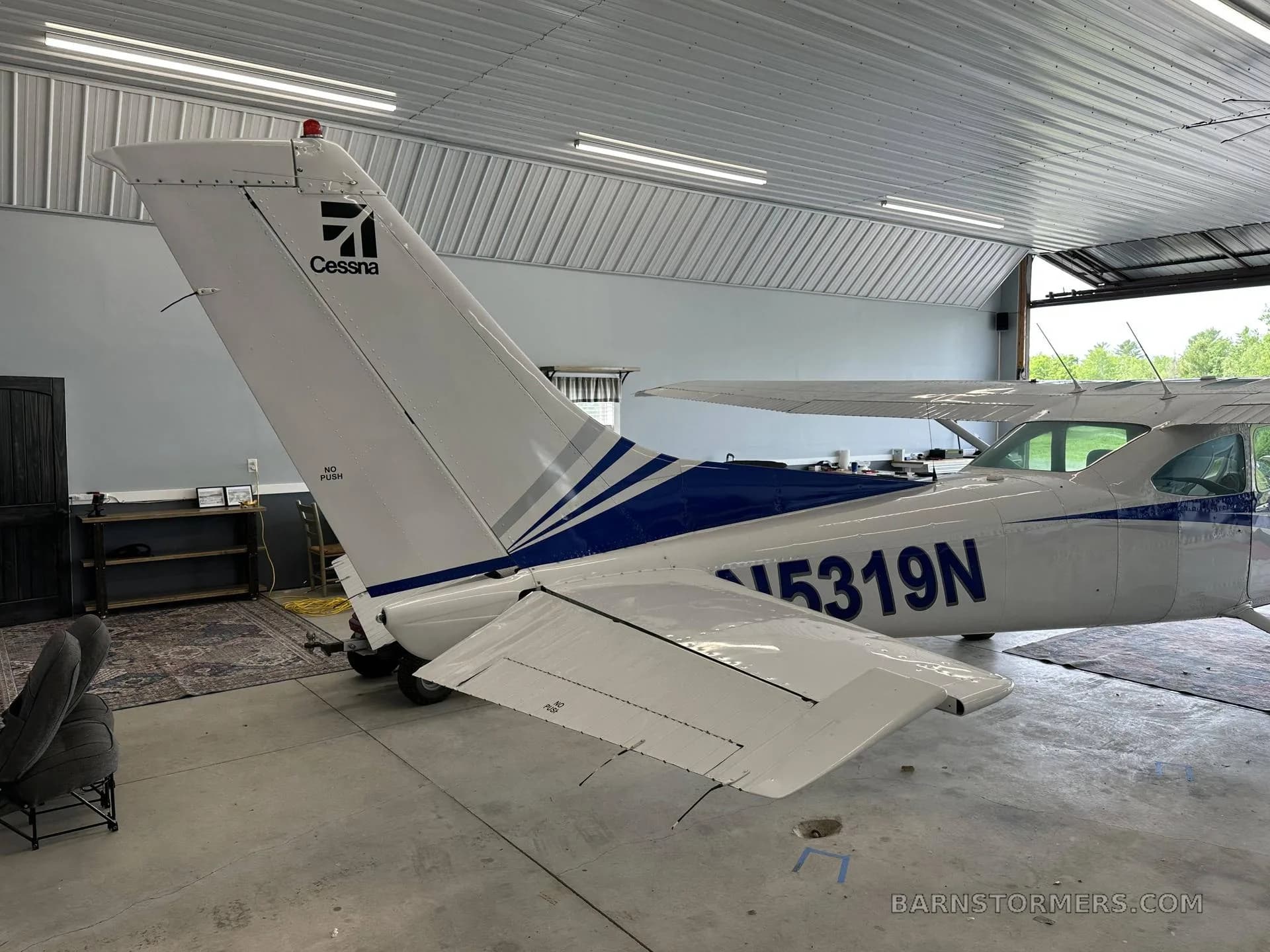 The tail section of a white and blue Cessna aircraft with registration N5319N is visible inside a hangar.