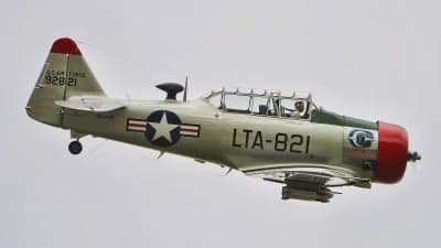 A T-6 Texan aircraft in flight with a silver and red paint scheme.