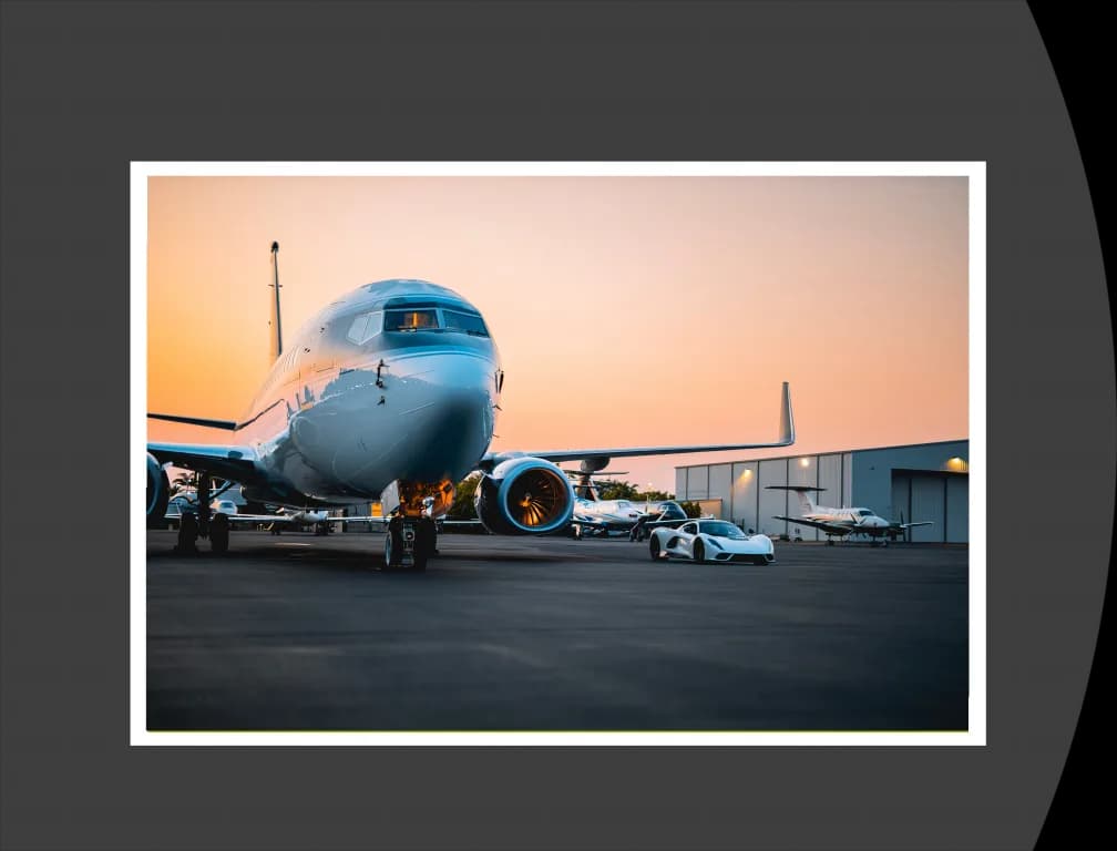 A Boeing 737 BBJ in a dark blue and white livery parked on an airfield at sunset, with a white sports car in front.
