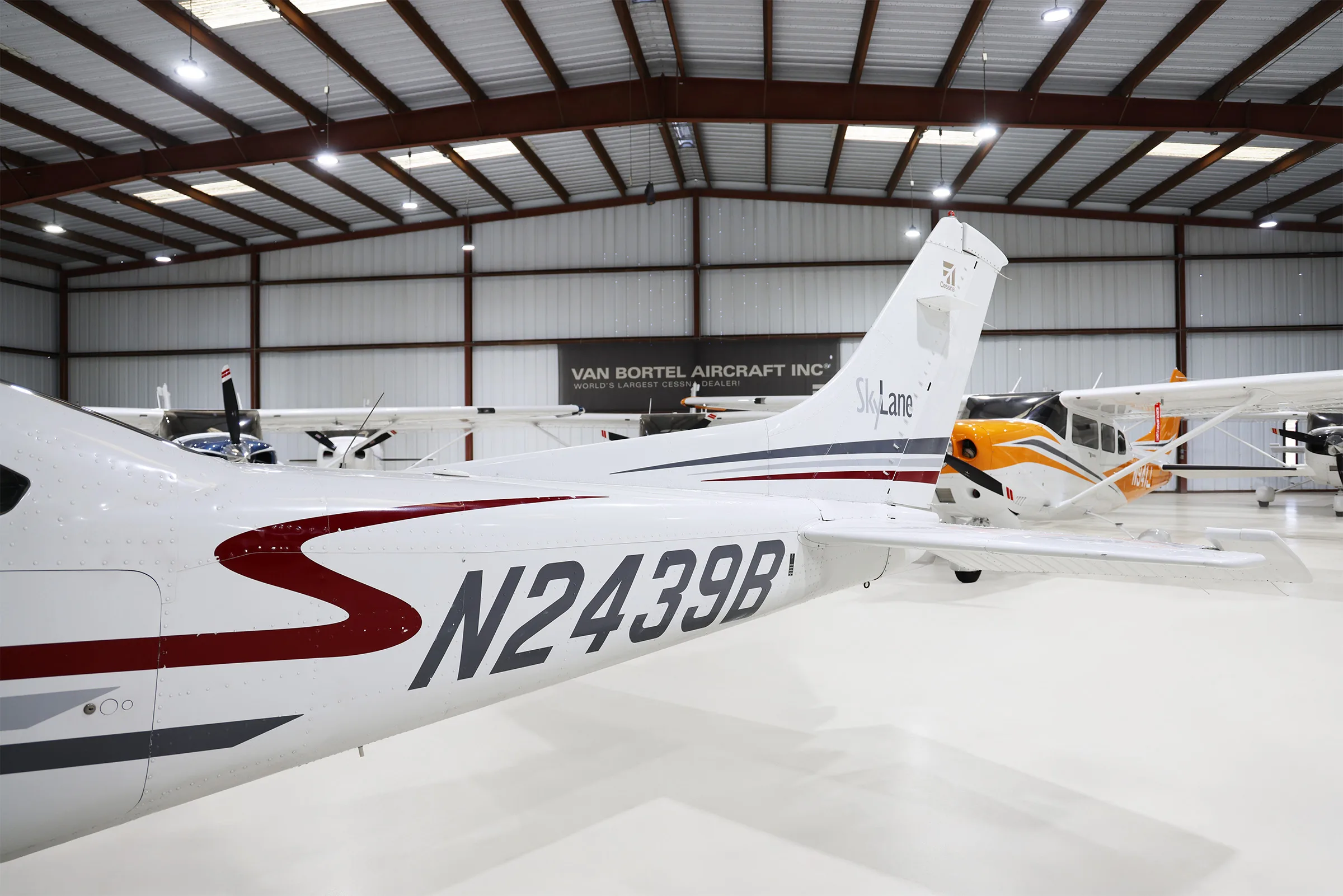 The tail section of a white Cessna 182 Skylane with red and grey stripes, showing the N2439B registration, in a hangar.