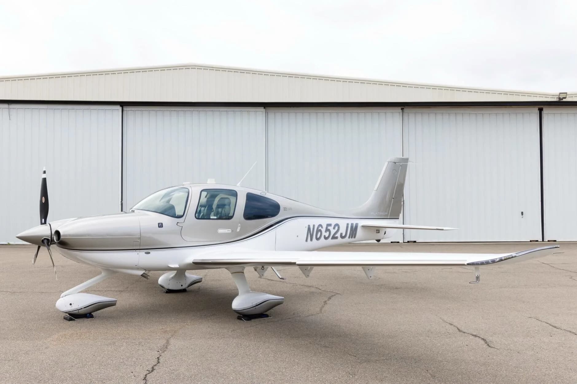 A side view of the silver and white Cirrus SR22 aircraft with N652JM registration, parked in front of hangars.