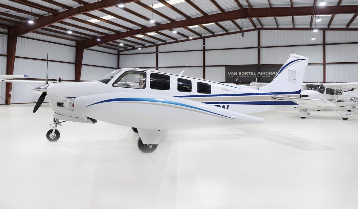 Side view of a white Beechcraft Bonanza N802PN with blue and grey stripes, parked in a hangar.